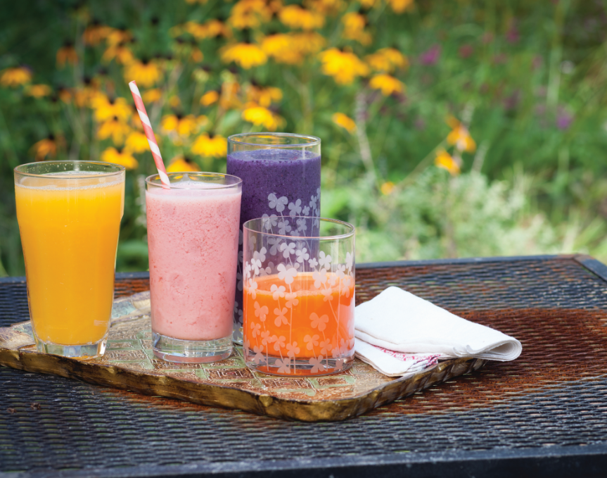 Four glasses on a tray filled with different colored juices and smoothies with best antioxidants for macular degeneration, including the Blueberry Banana Pomegranate Smoothie