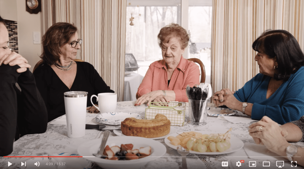 AMD patient Mary Toss sits at table with her four daughters. Coffee and food sits on the table as the women talk.